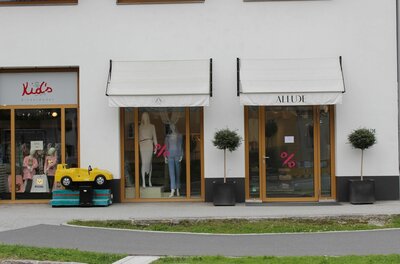 Allude Ladengeschäft Außenansicht des Bekleidungsgeschäfts Allude mit Schaufenstern, Markisen und einem gelben Kinder-Spielauto.