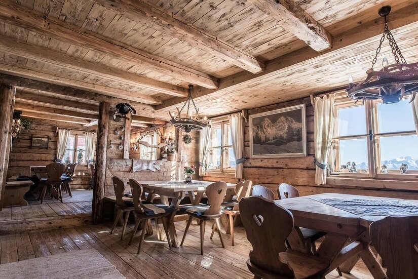 Gaststube Berggasthaus Resterhöhe Rustikale Gaststube aus hellem Holz mit Holztischen, Stühlen mit Herz-Ausschnitt und Geweih-Leuchtern.