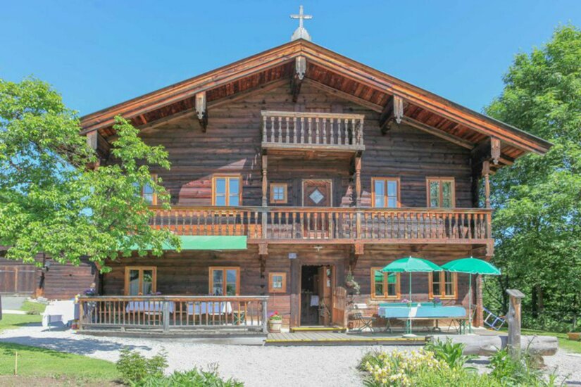 Zweistöckiges traditionelles Holzhaus mit Balkonen und Außengastronomie unter blauem Himmel.