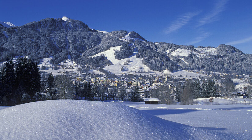 Verschneite Berglandschaft mit Blick auf Kitzbühel unter blauem Himmel.