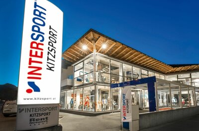 Intersport Kitzsport Filiale Beleuchtetes Sportgeschäft mit Glasfassade und großem Intersport-Werbeschild bei Dämmerung.