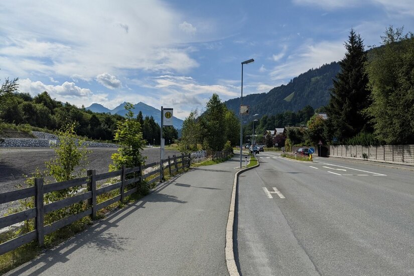 Bushaltestelle an einer asphaltierten Straße mit Bergen im Hintergrund.
