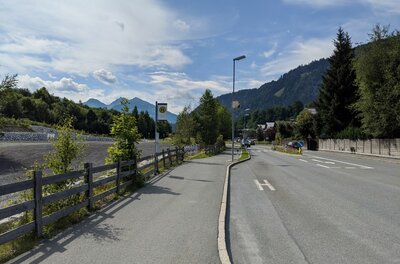 Bushaltestelle an einer asphaltierten Straße mit Bergen im Hintergrund.