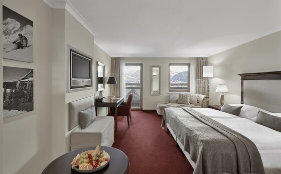 Modernes Hotelzimmer mit Doppelbett, rotem Teppichboden, Schreibtisch und Blick auf die Berge.