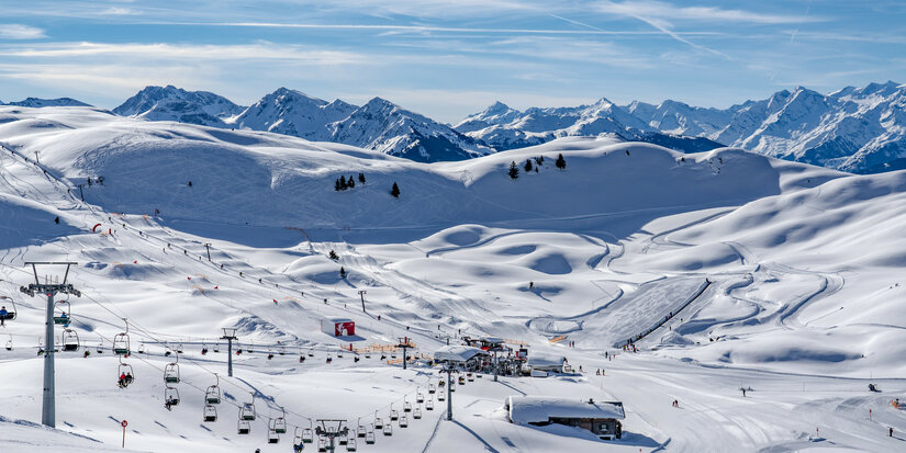 Eine schneebedeckte Winterlandschaft mit Skifahrern, Sesselliften und majestätischen Bergen im Hintergrund.