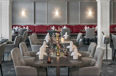 Eingedeckte Tische in einem Restaurant mit grauen Polstersesseln und roter Sitzbank.