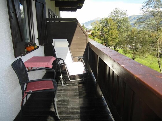 Holzbalkon mit Liegestuhl, Tisch und Stuhl vor einer Bergkulisse.
