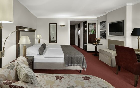 Modernes Hotelzimmer mit Doppelbett, rotem Teppichboden, Sitzecke und Fernseher.