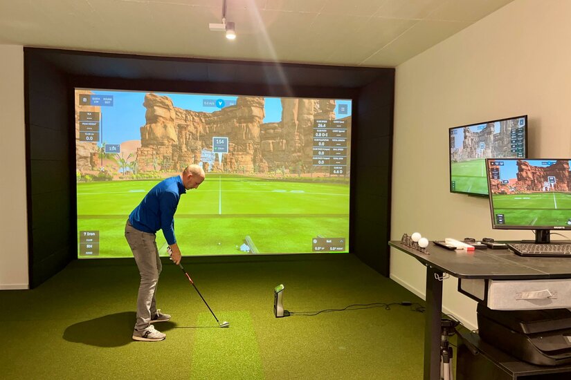 Golfsimulator Ein Mann spielt Golf in einem modernen Golf-Simulator. Die große Leinwand zeigt eine virtuelle Golflandschaft mit digitalen Statistiken.