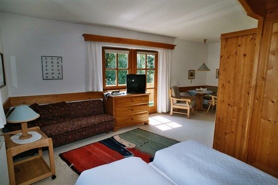 Zimmeransicht Ponapart GOLF & SCHI Innenansicht eines Hotelzimmers mit Sofa, Holzmöbeln, Fernseher und Betten im Vordergrund.
