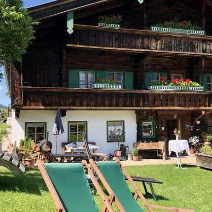 Ein traditionelles Holzhaus mit grünen Fensterläden, umgeben von blühenden Pflanzen und einer einladenden Gartenlandschaft.