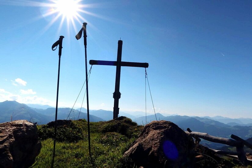 Gipfelkreuz bei der Bichlalm Gipfelkreuz und Wanderstöcke vor Gebirgspanorama bei Sonnenschein.