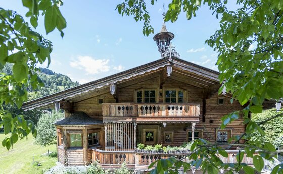 Traditionelles Holzhaus mit Balkonen und Glockenturm hinter grünen Blättern.