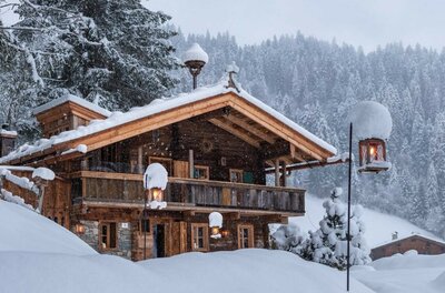 Verschneites Green Chalet Verschneites Holzhaus in den Alpen mit Laternen und Tannenwald im Hintergrund.