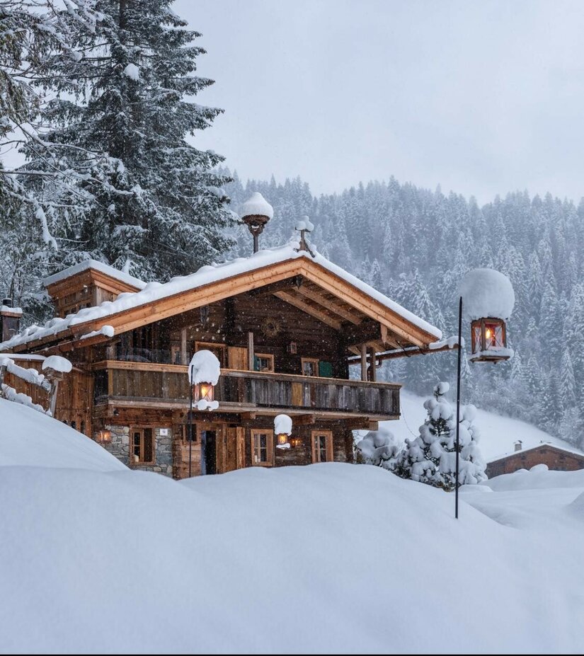 Verschneites Green Chalet Verschneites Holzhaus in den Alpen mit Laternen und Tannenwald im Hintergrund.