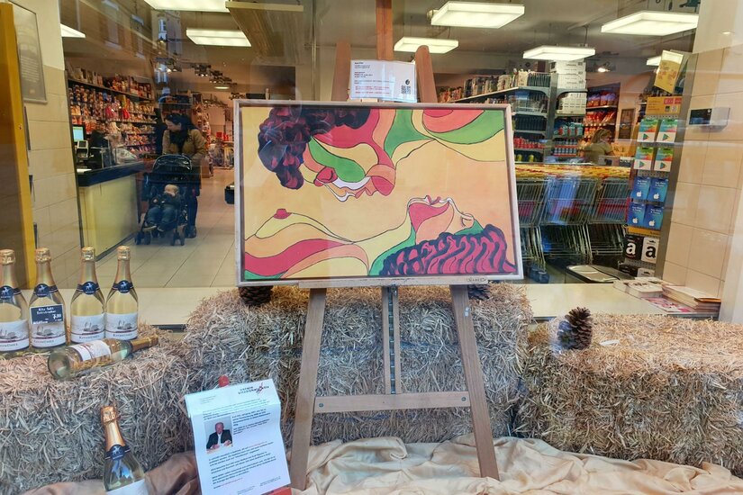 Billa Künstlerfenster Ein buntes Kunstwerk in einem Schaufenster, das zwei Profilgesichter zeigt. Darunter stehen Flaschen und dekoratives Stroh.