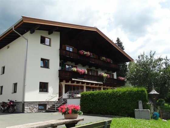 Außenansicht Gästehaus Wallner Mehrstöckiges Gästehaus mit Holzbalkonen, Blumenschmuck und einer Hecke im Vordergrund.