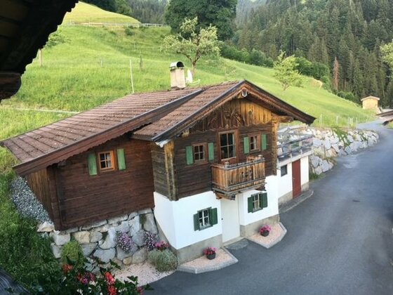 Hausansicht Bauernhof Sinnersberg Traditionelles Holzhaus mit weißem Sockel an einem asphaltierten Weg vor grünen Almwiesen.