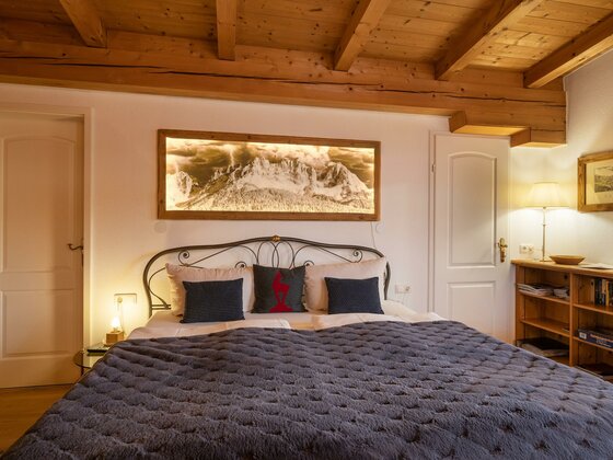 Das_Chalet_Kirchberger_Strasse_Kirchberg_Wohnraum_ Ein gemütliches Schlafzimmer mit einem großen Bett und Holzdecken. An der Wand hängt ein Kunstwerk, und es gibt warmes Licht, das eine einladende Atmosphäre schafft.
