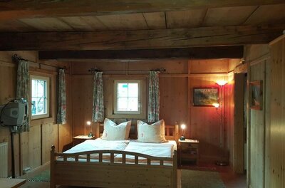 Rustikales Schlafzimmer mit Holzwänden, Doppelbett und Deckenbalken im Angererhof.
