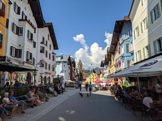 Fußgängerzone in Kitzbühel mit farbigen Häuserfassaden und Außengastronomie unter blauem Himmel.