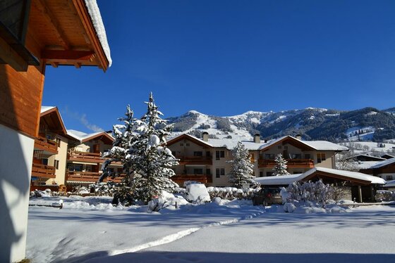 Hotel Aurach im Winter Verschneite Hotelanlage mit Holzbalkonen vor bewaldeten Bergen unter blauem Himmel.
