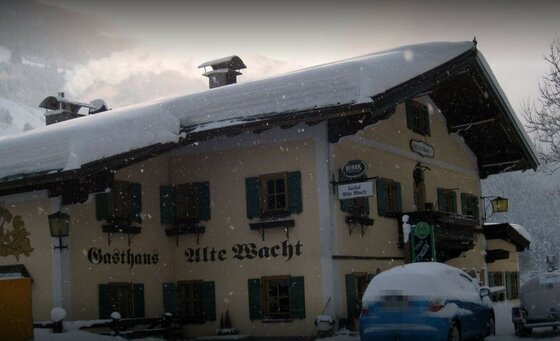 Gasthaus Alte Wacht im Winter Verschneites Gasthaus Alte Wacht mit schneebedecktem Satteldach und dunklen Fensterläden bei leichtem Schneefall.