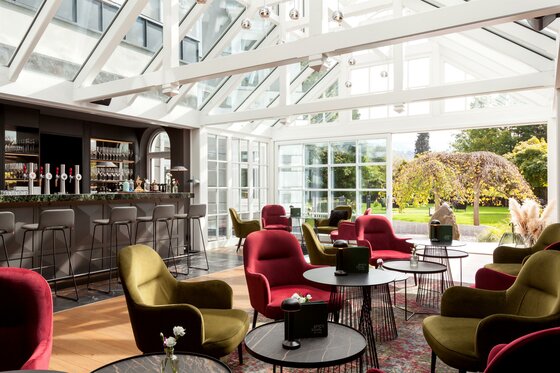 Moderner Wintergarten mit Bar, roten und grünen Sesseln sowie Blick in den Garten.