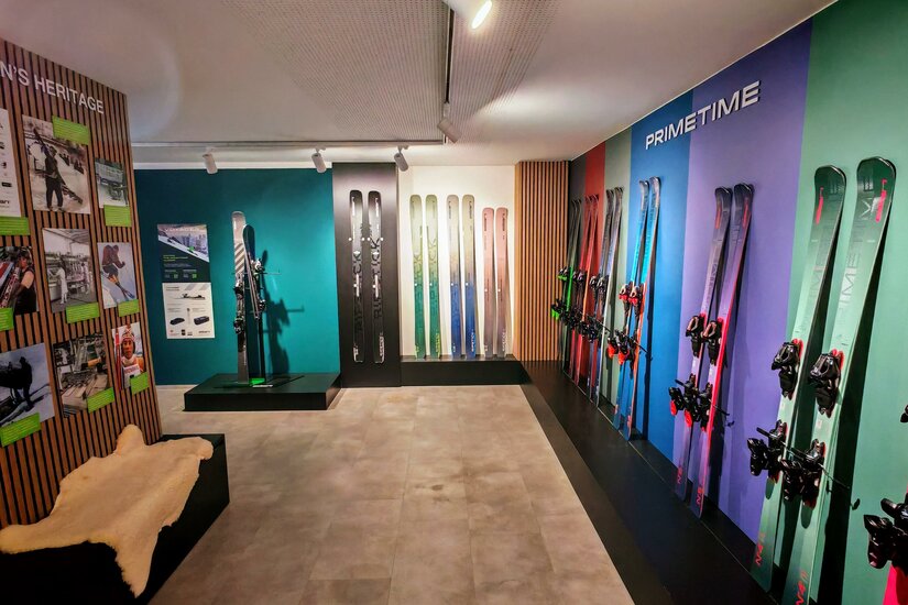 Kjus & Elan Brand Store Ein moderner Ausstellungsraum mit verschiedenen Skiern an der Wand. Die Wände sind bunt gestaltet und es gibt Informationsmaterial über die Produkte.