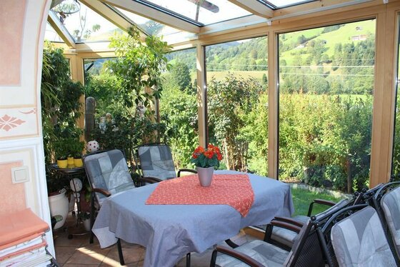 Wintergarten im Haus Kreidl Ein heller Wintergarten mit Esstisch, Stühlen und Blick auf grüne Berghänge.
