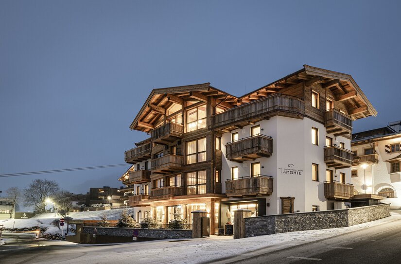 LaMonte Bistro und Unterkunft Mehrstöckiges alpines Gebäude mit Holzfassade und beleuchteten Fenstern in der Dämmerung bei Schnee.