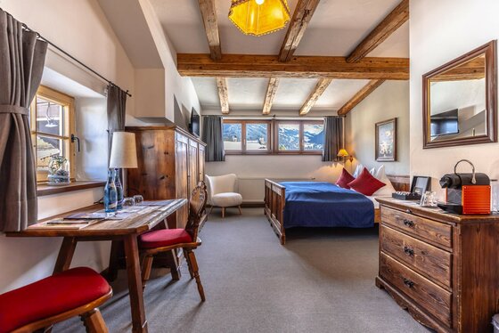 Rustikales Hotelzimmer mit Holzmöbeln, Doppelbett, Holzbalkendecke und Fenster mit Bergblick.