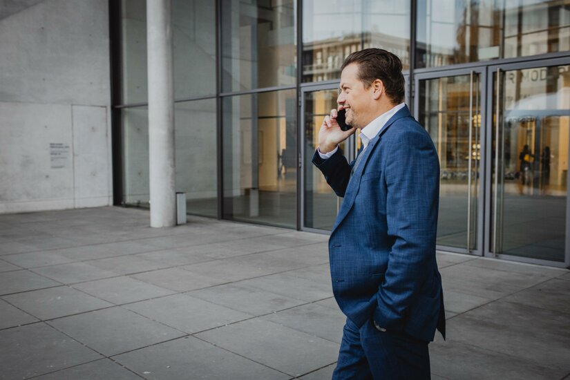 <p>Ein geschäftlich gekleideter Mann telefoniert lächelnd vor einem modernen Gebäude.</p>