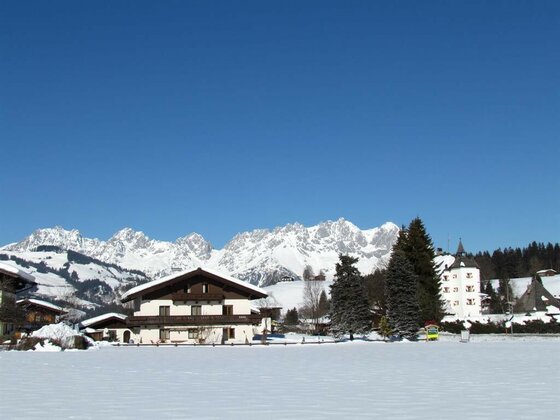 Verschneites Alpenhaus vor dem Gebirgsmassiv des Wilden Kaisers unter blauem Himmel.