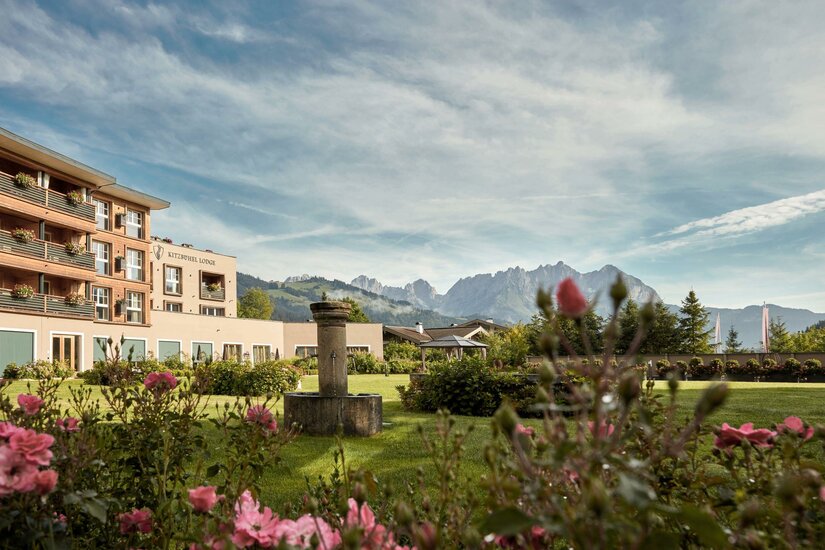 Exterior View Kitzbühel Lodge Außenansicht der Kitzbühel Lodge mit Gartenanlage, Steinbrunnen und Blick auf das Gebirge Wilder Kaiser.