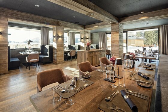 Moderner Restaurantraum mit Holzwänden, eingedeckten Tischen und großen Fensterfronten.