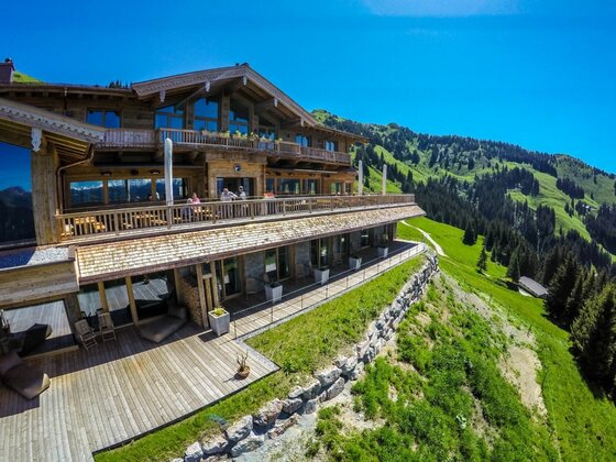 Terrasse der Bichlalm Große Holzterrasse der Bichlalm vor einem bewaldeten Berghang unter blauem Himmel.