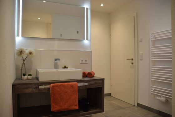 Modernes Badezimmer mit weißem Aufsatzwaschbecken, großem Leuchtspiegel und Handtuchheizkörper.