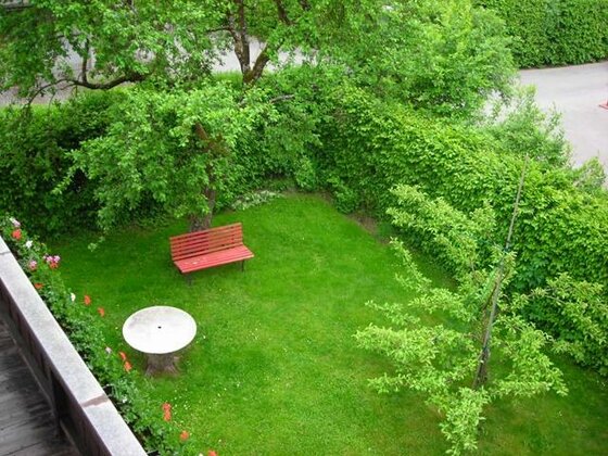 Blick von oben auf einen grünen Garten mit roter Holzbank, rundem Steintisch und hohen Hecken.
