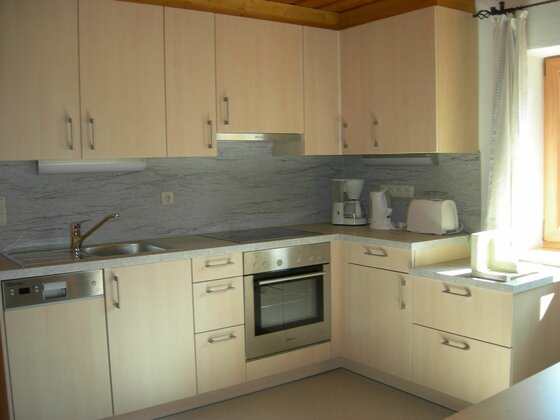 Moderne Einbauküche in L-Form mit hellen Holzfronten, Herd, Backofen und Kaffeemaschine.