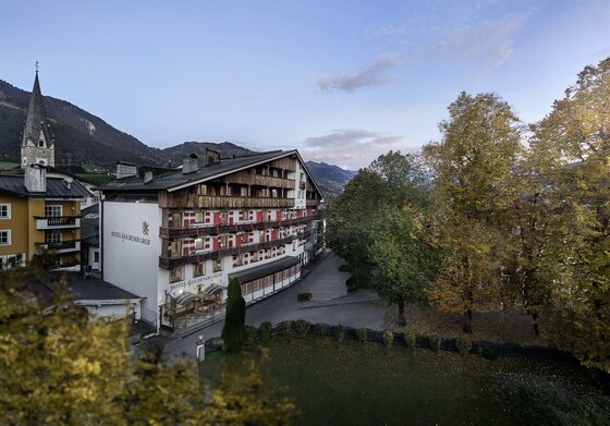 Außenansicht des Hotel Goldener Greif mit Holzbalkonen vor herbstlichen Bäumen und Bergen.