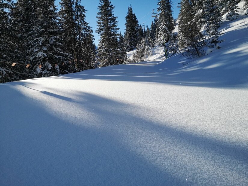 Winterlandschaft bei St. Bernhard Kapelle Verschneite Skipiste oder Wanderweg im Nadelwald unter blauem Himmel.