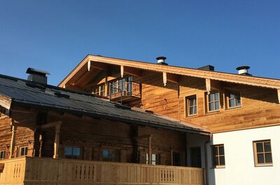 Außenansicht eines traditionellen Holzgebäudes mit Balkon und Satteldach unter blauem Himmel.