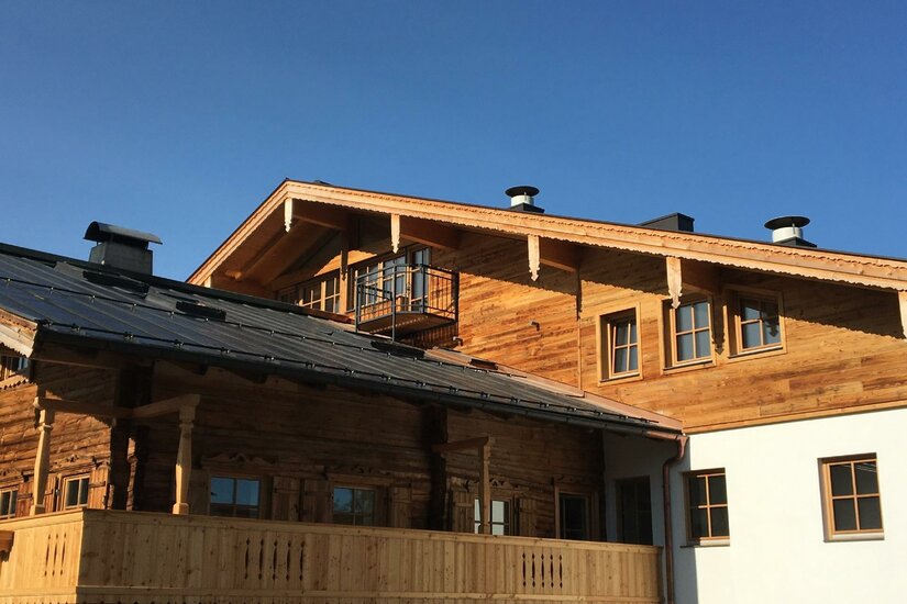 Außenansicht eines traditionellen Holzgebäudes mit Balkon und Satteldach unter blauem Himmel.
