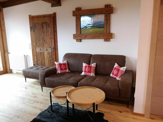 Braunes Sofa mit rot-weiß karierten Kissen vor einer weißen Wand mit Holzbild und Holztür.