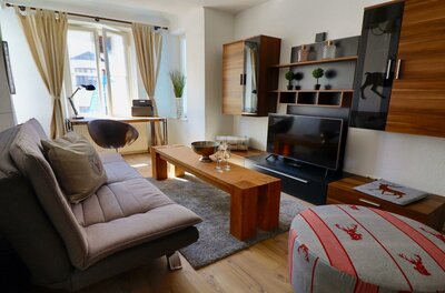 Modernes Wohnzimmer mit Sofa, Holztisch, Fernseher und Schreibtisch am Fenster.