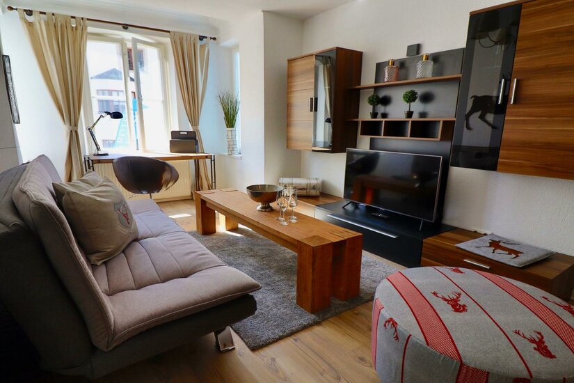 Modernes Wohnzimmer mit Sofa, Holztisch, Fernseher und Schreibtisch am Fenster.