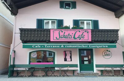 Rosa Fassade des Schatzi Cafés in Kitzbühel mit grünen Fensterläden und Außenbestuhlung.