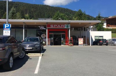 Eingangsbereich eines Spar-Supermarktes mit Parkplatz und bewaldetem Berg im Hintergrund.