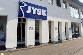 Außenansicht einer JYSK-Filiale mit blauem Logo an einer weißen Fassade.